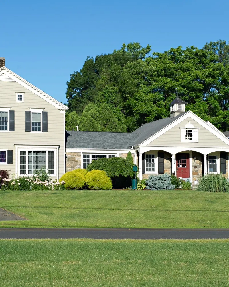 Cream colonial building with red doors, a covered porch and a sign, set behind a green lawn on a sunny day