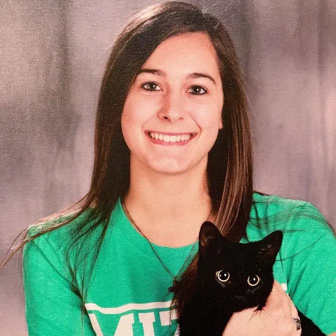 Smiling young woman in a green shirt holding a black cat