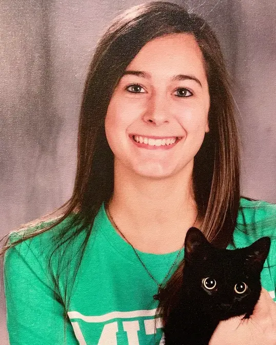 Smiling young woman in a green shirt holding a black cat