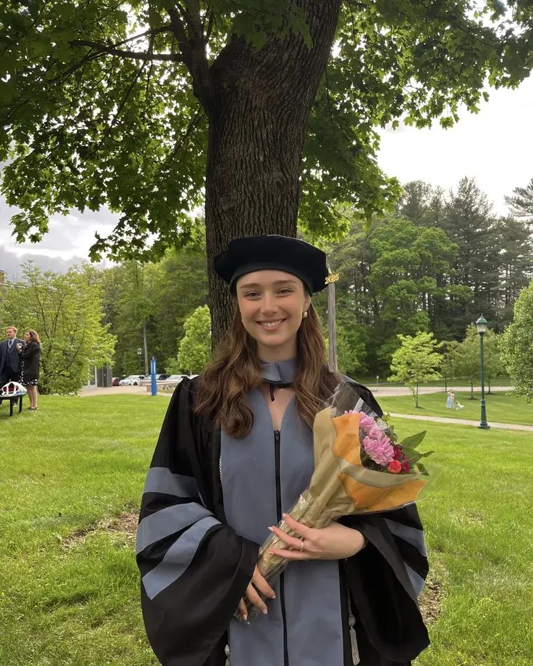 Tara Francis, DVM, MS: Smiling woman in a doctoral graduation gown and cap holding a bouquet under a large tree